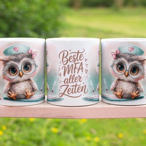 May include: Three white ceramic mugs with a cute owl design. The owl wears a nurse's cap and glasses. The middle mug has the text "Beste MFA aller Zeiten". The mugs are on a pink surface with a blurred green background.
