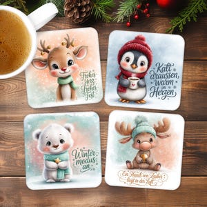 Op de afbeelding: Set van vier vierkante keramische onderzetters met winterthema-illustraties. Ontwerpen omvatten een rendier, pinguïn, ijsbeer en eland, elk met feestelijke kleding en Duitse tekst. Een kopje koffie staat in de linkerbovenhoek.