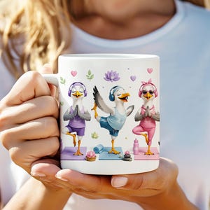 May include: A white ceramic mug featuring a graphic illustration of three seagulls performing yoga poses. The seagulls wear colorful athletic clothing, headphones, and sunglasses, while practicing on individual mats with lotus flowers and water bottles.