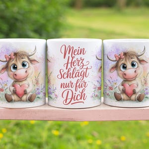 Può includere: Tre tazze in ceramica bianca con un disegno di mucca dei cartoni animati. La mucca tiene in mano un cuore rosa ed è circondata da fiori. La tazza centrale ha il testo "Mein Herz schlägt nur für Dich" in rosso.