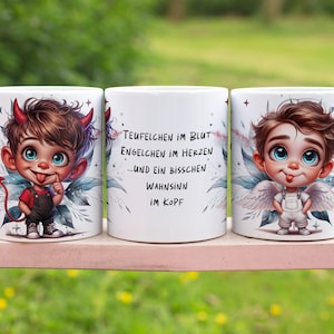 Op de afbeelding: Twee witte keramische mokken met een cartoonillustratie van een duivel en een engel. De mokken hebben een zwart handvat en de tekst "Teufelchen im Blut Engelchen im Herzen...und ein bisschen Wahnsinn im Kopf" staat op de voorkant van de mok.