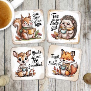 Könnte beinhalten: Set aus vier quadratischen Untersetzern mit Cartoon-Tierillustrationen. Jeder Untersetzer zeigt ein anderes Tier: ein Eichhörnchen, einen Igel, ein Reh und einen Fuchs, die jeweils eine Tasse Tee halten. Deutscher Text ist enthalten.