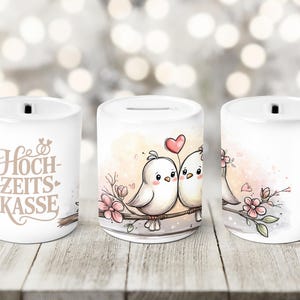 Può includere: Salvadanai in ceramica bianca con una fessura sulla parte superiore. La banca presenta un disegno di due uccelli dei cartoni animati su un ramo con fiori rosa e un cuore. Il testo "Hochzeits Kasse" è sul lato.