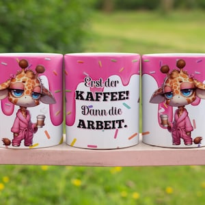 Op de afbeelding: Drie roze koffiemokken met een giraffenontwerp en de tekst "Erst der Kaffee! Dann die Arbeit." De giraffen dragen roze badjassen en houden kopjes koffie vast.