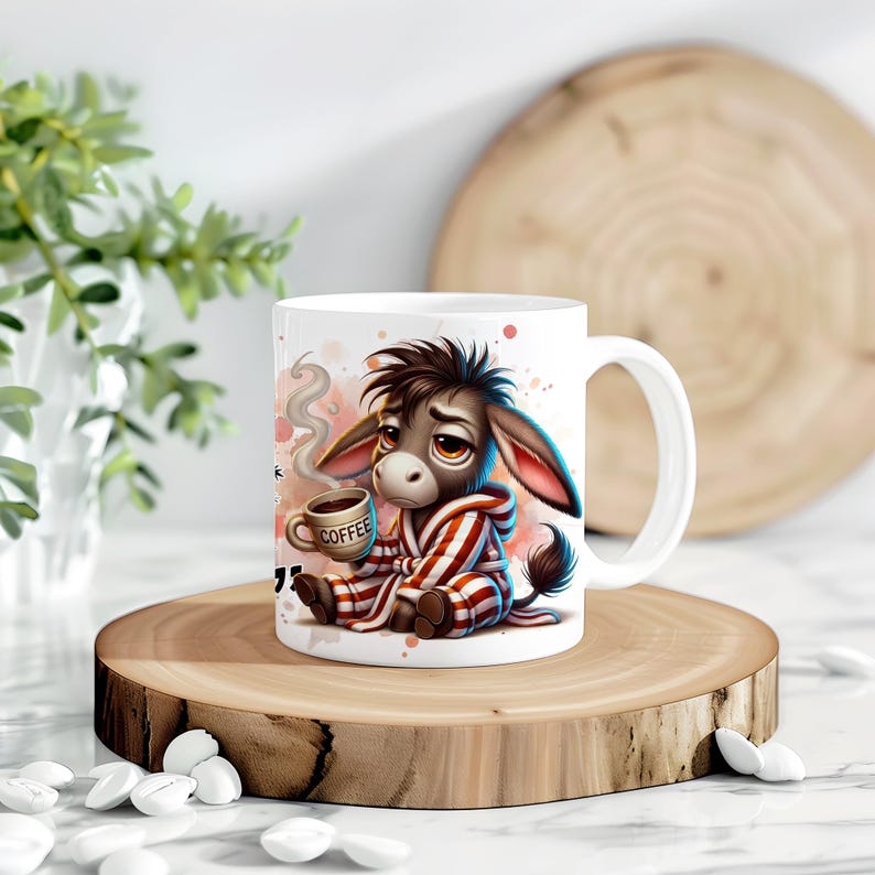 May include: White ceramic mug with a cartoon donkey wearing a red and white striped robe and holding a coffee cup. The donkey has a sad expression and the mug has the word "Coffee" written on the cup. The background is a watercolor-style design with pink and blue colors.