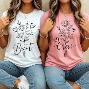 Puede incluir: Dos mujeres con camisetas a juego. Una camiseta es blanca con un diseño floral negro y la palabra "Braut". La otra camiseta es rosa con un diseño floral similar y la palabra "Crew". Ambas camisetas tienen cuello redondo.