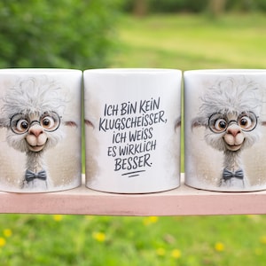 Puede incluir: Tres tazas de cerámica blanca con una llama de dibujos animados con gafas y pajarita. La taza central tiene texto en alemán. La llama tiene una cabeza gris y esponjosa y una cara sonriente. Las tazas están sobre una superficie rosa.