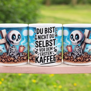 Könnte beinhalten: Drei weiße Keramik-Kaffeetassen mit einem blauen und weißen Design. Die Tassen zeigen ein Skelett, das eine Tasse Kaffee hält und auf einem Haufen Kaffeebohnen sitzt. Die mittlere Tasse hat den Text "Du bist nicht du selbst vor dem ersten Kaffee" in Schwarz.