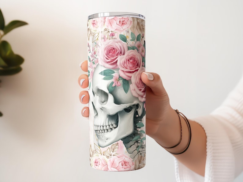 Pu&ograve; includere: Un bicchiere in acciaio inossidabile bianco con un design floreale che presenta un teschio con rose rosa e foglie verdi.