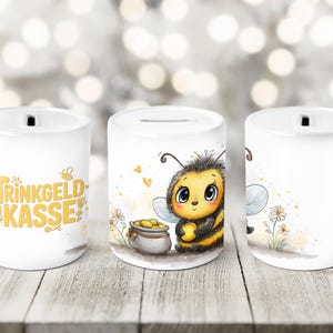 Könnte beinhalten: Weiße Keramik-Spardose mit einem Schlitz oben. Die Spardose zeigt ein Cartoon-Bienen-Design mit einem Topf voller Gold und dem Text "Trinkgeld Kasse" in Gelb. Die Spardose ist zylindrisch und hat eine glatte Oberfläche.