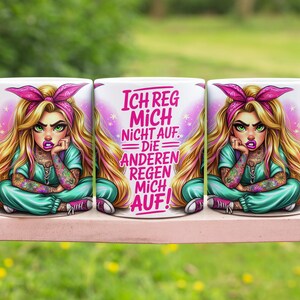 May include: White ceramic mug featuring a cartoon illustration of a woman with blonde hair, a pink bow, and tattoos. The mug has the text "ICH REG MICH NICHT AUF. DIE ANDEREN REGEN MICH AUF!" in pink and white.