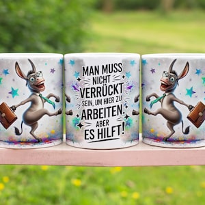Könnte beinhalten: Drei weiße Keramikbecher mit einem Cartoon-Esel-Design. Der Esel trägt eine Brille, eine Krawatte und eine Aktentasche. Die Becher haben den Text "MAN MUSS NICHT VERRÜCKT SEIN, UM HIER ZU ARBEITEN. ABER ES HILFT!" und bunte Sternakzente.