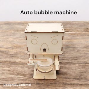 May include: A wooden toy bubble machine shaped like a robot with a surprised expression. The machine has a small glass container for bubble solution and a wand that dips into the solution.