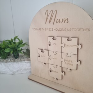 May include: Wooden sign with a puzzle design that says "Mum you are the piece holding us together." The puzzle pieces are labelled with names: Joe, Charlotte, Dad, Mum, Marie-Sophie, and Elena.