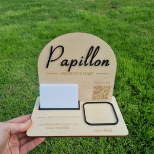 May include: A light-coloured wooden display stand with an arched top featuring the black text Papillon MAKEUP & HAIR. It includes a white card holder, a QR code, and a black square frame with the text TAP HERE, plus contact information.
