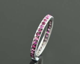 May include: A silver band ring with a row of pink gemstones around the entire band.