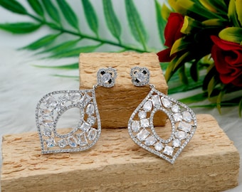 May include: A pair of silver dangle earrings with a geometric design. The earrings are adorned with clear cubic zirconia stones.