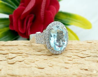 May include: A silver ring with a large oval-shaped blue gemstone surrounded by smaller clear gemstones.