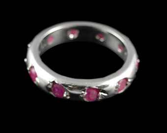 May include: A silver band ring with a row of pink ruby stones set around the band.