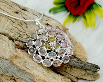 May include: A silver necklace with a round pendant featuring a cluster of oval-shaped gemstones in shades of pink, yellow, and green. The pendant is surrounded by smaller, clear gemstones.