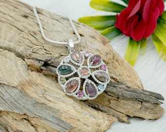 May include: A silver necklace with a round pendant featuring a floral design with multi-colored gemstones. The pendant is set with a variety of gemstones, including pink, green, blue, and clear stones.
