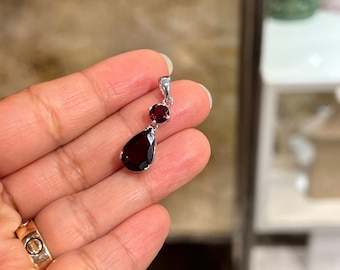 Può includere: Un ciondolo d'argento con tre pietre preziose rosse. Il ciondolo presenta una pietra a forma di lacrima, una pietra rotonda e una pietra rotonda più piccola.