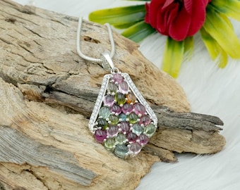 May include: A silver pendant necklace with a teardrop-shaped design featuring a cluster of multi-colored gemstones. The pendant is surrounded by a border of smaller, clear gemstones.