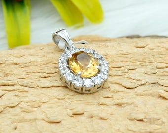 May include: A silver pendant with a large oval-shaped yellow gemstone surrounded by smaller white gemstones.