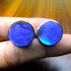 Puede incluir: Dos cabujones redondos de labradorita iridiscente de color azul y morado. Los cabujones tienen un diámetro de aproximadamente 2,5 cm.
