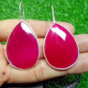 Può includere: Un paio di orecchini pendenti con una pietra preziosa rosa a forma di lacrima incastonata in una cornice argentata.