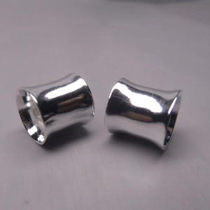 May include: Two silver metal ear gauges, each with a slightly flared, cylindrical shape.