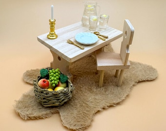 Può includere: Un set da tavolo e sedia in legno in miniatura con un piatto bianco, posate d'oro, una caraffa e bicchieri d'acqua, un candelabro e un cesto di frutta su un tappeto marrone.