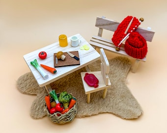 Può includere: Un set da tavolo in legno in miniatura con un pomodoro rosso, carote, un porro, un fungo, un coltello, un bicchiere, una tazza e un cesto di verdure. Sono inclusi anche una sedia e una panca in legno in miniatura.