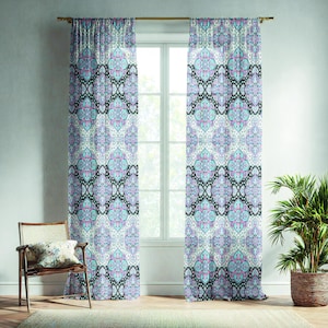 May include: Two patterned window curtains with a repeating design in shades of blue, purple, and black. The curtains hang in front of a window, with a wooden chair and a potted plant visible in the room. The curtains are hung on a gold-colored rod.