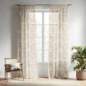 Puede incluir: Dos cortinas beige y blancas estampadas cuelgan frente a una ventana. Las cortinas tienen un diseño geométrico de diamantes. Una silla de madera con un cojín y una planta en maceta están frente a las cortinas.