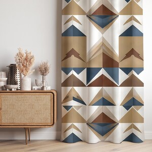 May include: Geometric patterned curtain featuring a repeating design of triangles and diamond shapes in shades of blue, brown, and beige. The curtain is hanging in front of a white wall, with a wooden cabinet and decorative items visible on the left.