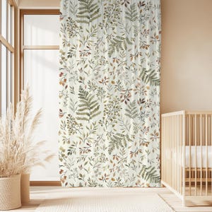 May include: Cream-coloured curtain featuring a botanical pattern of green, brown, and grey leaves and ferns. The curtain hangs in front of a window, with a baby cot visible on the right. The curtain is made of a soft, flowing fabric.
