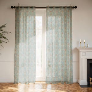 May include: Two sheer, light blue curtains with a repeating floral pattern in peach and white hang in front of a window. The curtains are hung on a dark rod. The room has a fireplace and hardwood floors.
