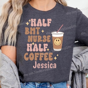 May include: Dark grey heather t-shirt with the text "HALF BMT NURSE HALF COFFEE Jessica" in pink and brown lettering. A coffee cup with a smiley face is also featured on the shirt.