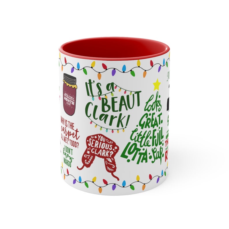 May include: White ceramic mug with a red interior, featuring quotes and phrases from a holiday movie. The mug has a festive design with colorful string lights and text in various fonts and colors, including "It's a beaut, Clark!"