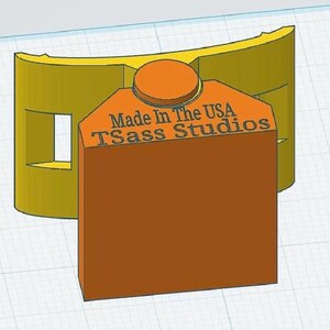 May include: A 3D-printed object featuring a curved yellow base with rectangular cutouts and an attached orange rectangular block. The orange block displays the embossed text Made In The USA and TSass Studios with a circular top detail.