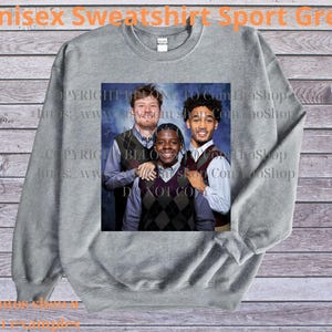 May include: A gray unisex sweatshirt with a printed image of three people. The image is centered on the front of the sweatshirt. The text "Unisex Sweatshirt Sport Grey" is printed at the top of the image.