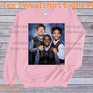 May include: Light pink unisex sweatshirt with a graphic of three people. The sweatshirt has the text "Unisex Sweatshirt Light Pink" at the top. The image on the sweatshirt is a group photo of three people wearing vests and collared shirts.