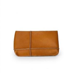 May include: A rectangular, tan leather clutch with rounded corners. The clutch is stitched around the edges and features a decorative, woven tan leather design across the front. The bag is empty and sits against a white background.