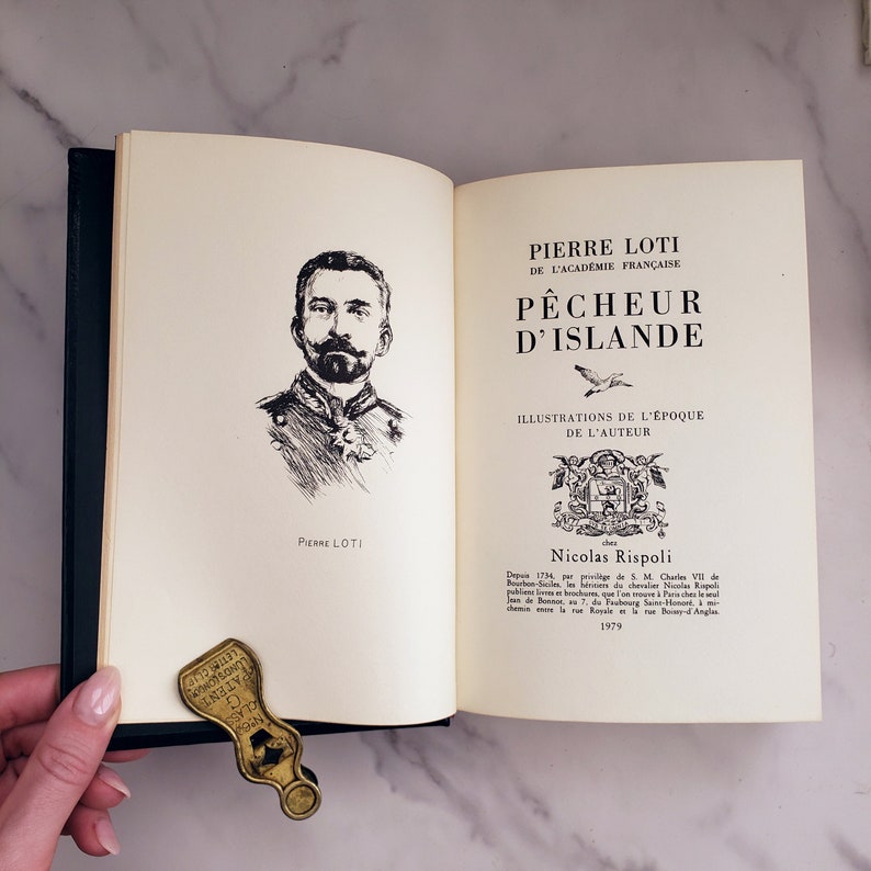 Może przedstawiać: Antyczna książka zatytułowana "P&ecirc;cheur d'Islande" autorstwa Pierre'a Lotiego, ilustrowana przez Nicolasa Rispoliego. Okładka książki przedstawia czarno-białą ilustrację mężczyzny z wąsami i brodą, ubranego w mundur wojskowy.