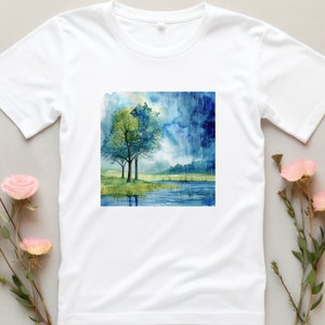 May include: White t-shirt with a watercolor painting of two trees by a lake with a stormy sky in the background.