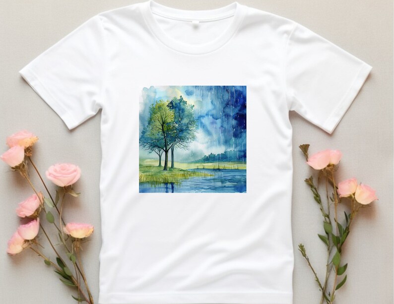 May include: White t-shirt with a watercolor painting of two trees by a lake with a stormy sky in the background.