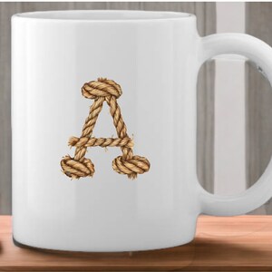 May include: White ceramic mug with a rope-style letter A design. The letter is made of brown rope and is centered on the mug.