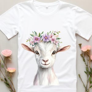 May include: White t-shirt with a watercolor illustration of a goat wearing a flower crown. The goat has a white face with pink accents and a pink nose. The flowers in the crown are pink and purple.