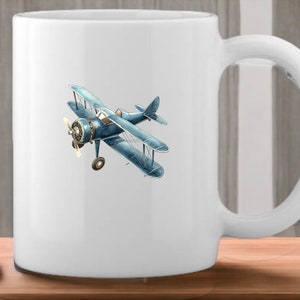 Op de afbeelding: Witte keramische mok met een illustratie van een blauw en wit vintage vliegtuig.